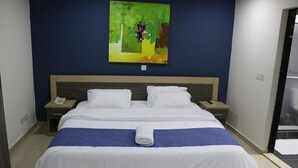 A hotel room with a large bed, two bedside tables, a painting on the wall, and a bathroom door visible. - The Cate House Hotel (Lagos)