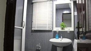 A bathroom with a toilet, a sink, a mirror, and a window with blinds. - The Cate House Hotel (Lagos)