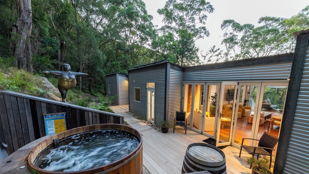 Een modern terras buiten met een hottub, houten vaten en een zithoek met uitzicht op het omliggende bos.