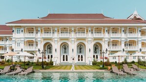 Un grande edificio a più piani con un ingresso centrale, balconi e una piscina di fronte.