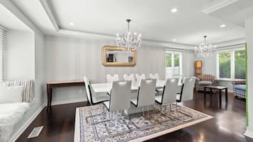 A dining area with a large table, white chairs, and a chandelier.