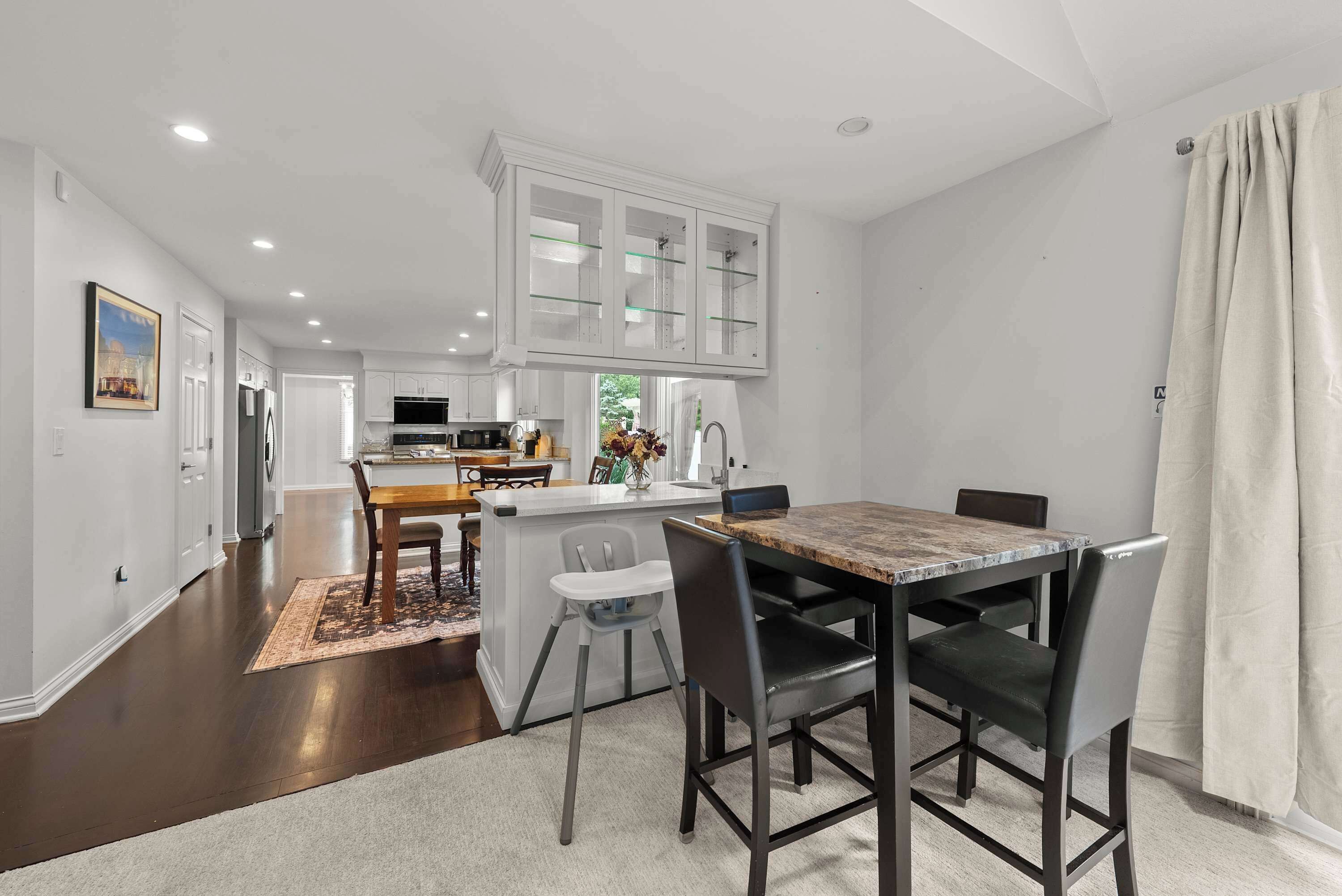 A modern kitchen with white cabinets, a central island, and a dining area with a marble table and chairs.