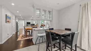 Una cocina moderna con armarios blancos, una isla central y un comedor con una mesa y sillas de mármol.
