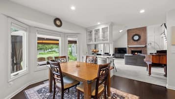 Un comedor con mesa y sillas de madera, una cocina con armarios blancos, una chimenea y un piano.