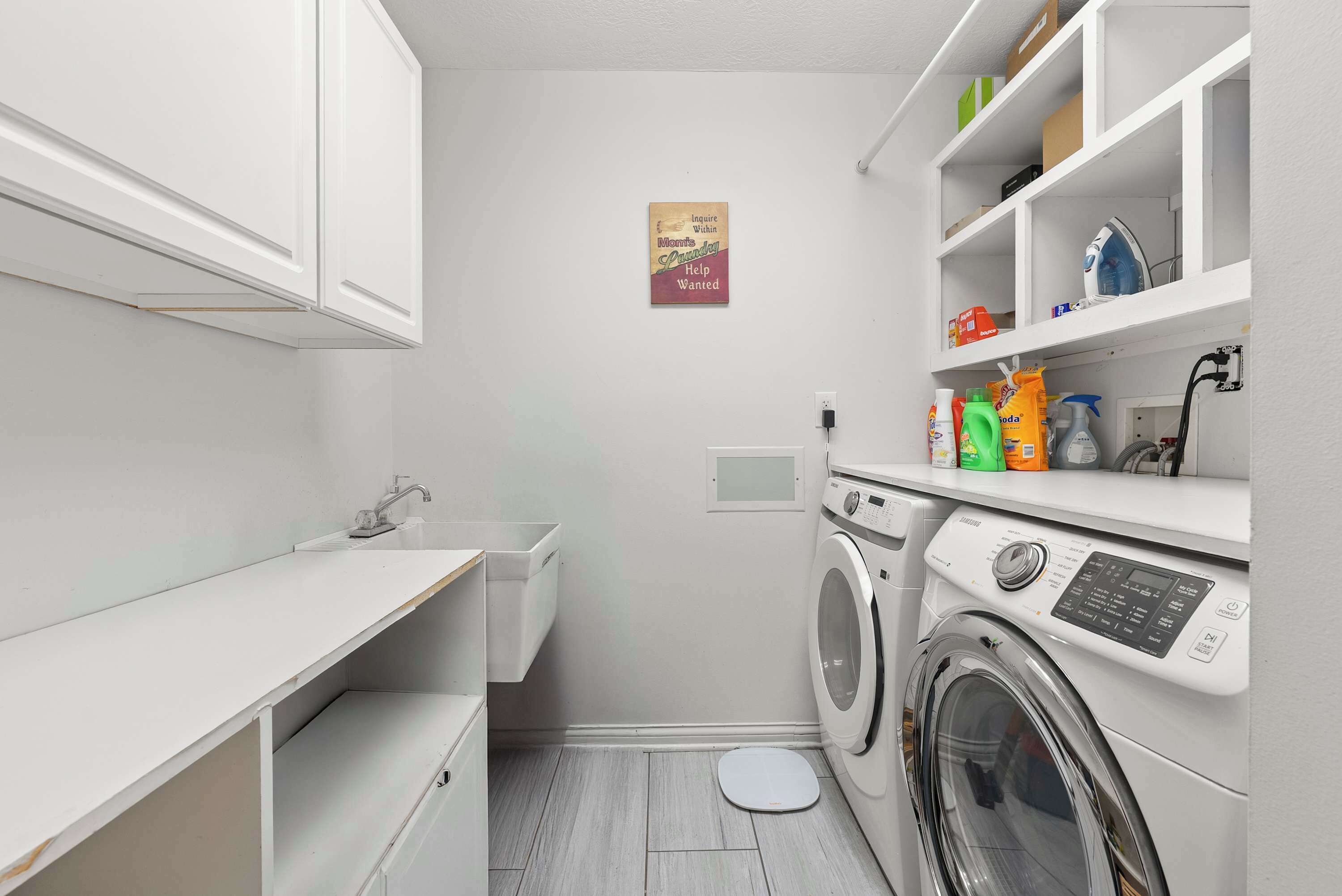 A compact laundry room with a washing machine, a sink, and shelves with cleaning supplies.