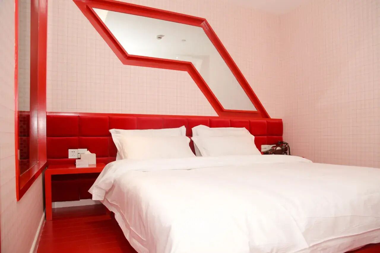 Een bed met witte beddengoed, een rood hoofdeinde en een spiegel aan de muur.