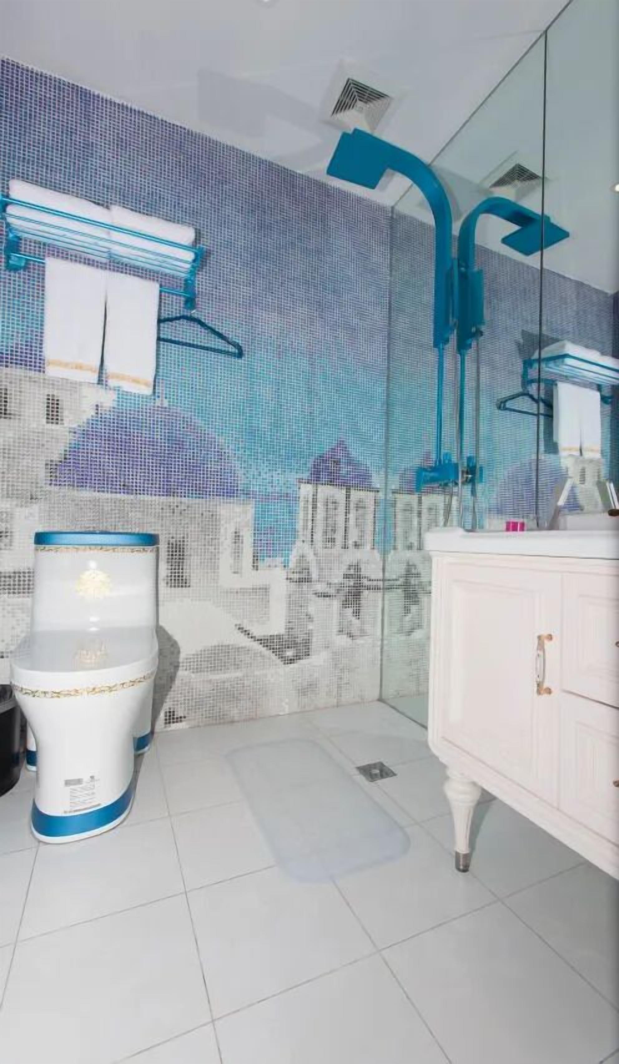 A bathroom with a modern design, featuring a white toilet, a white vanity with a mirror, and a blue showerhead.