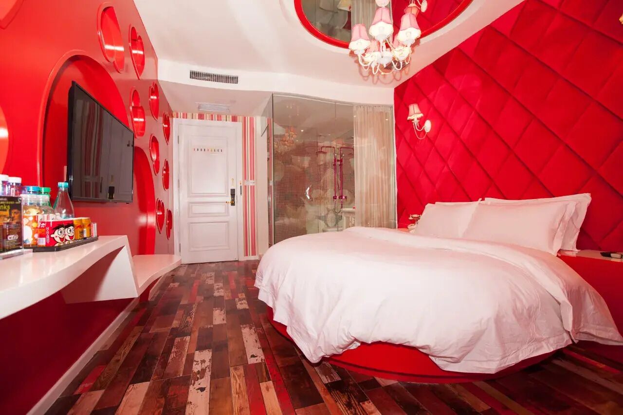 A modern bedroom with a red and white color scheme, a large bed, a vanity with toiletries, and a television on the wall.