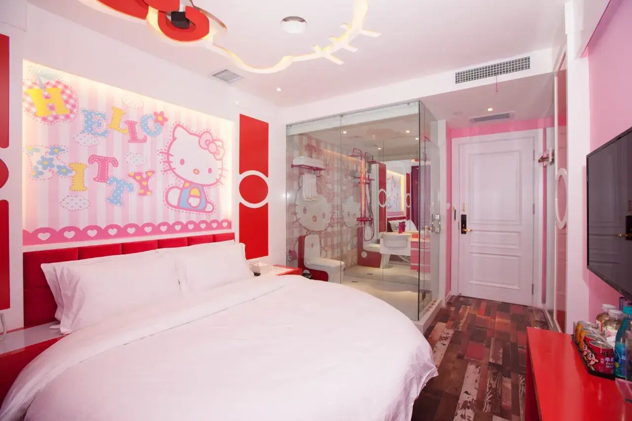 Habitación de hotel moderna con una cama grande, zona de ducha con mampara de vidrio y una decoración en tonos rosa y blanco.