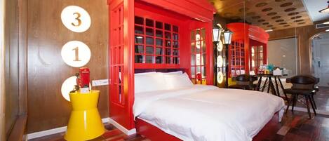 A room with a large bed, a red telephone booth-like structure, and a yellow side table.