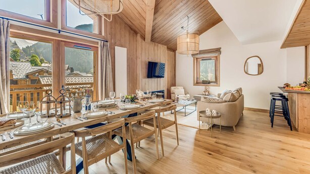 Un comedor espacioso con una mesa de madera dispuesta para una comida, una zona de estar acogedora con un sofá y sillas, y un área de cocina con una barra.