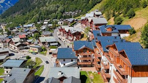 Un pueblo montañoso con casas de madera tradicionales, un camino sinuoso y un denso bosque y montañas al fondo.