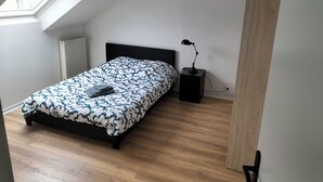 Ein Schlafzimmer mit einem Bett, einem Nachttisch, einer Lampe, einer Heizung und einem Dachfenster.