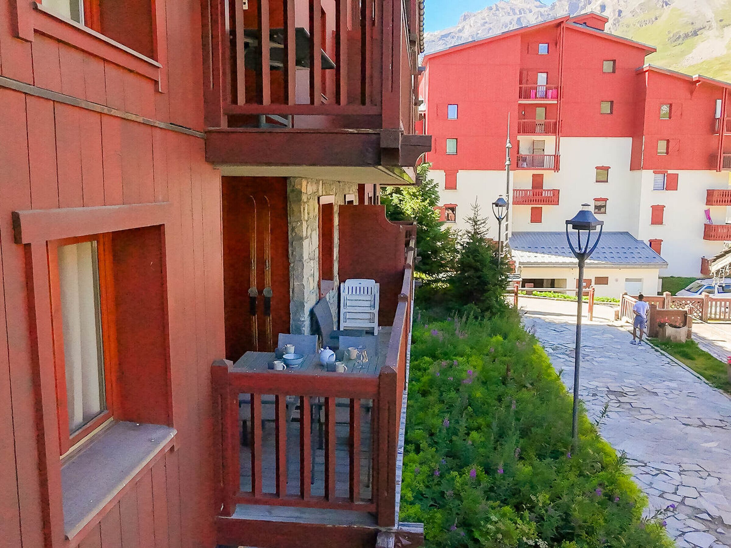 Un edifici vermell amb un balcó, un camí de pedra i una muntanya al fons.