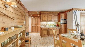 Un intérieur en bois comprenant un coin cuisine, avec une table à manger dressée, agrémentée de verres à vin et d’assiettes, ainsi qu’une étagère contenant divers ustensiles de cuisine.