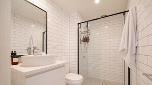 A modern bathroom with white subway tiles, a glass-enclosed shower, a white sink, and a toilet.
