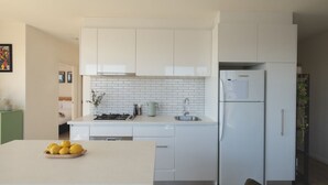A modern kitchen with white cabinets, a white countertop, a built-in stove, and a refrigerator.