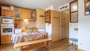 A compact kitchen with wooden cabinets, a dining table with a floral tablecloth, and a bench. - Studio cabin 3 pers South balcony on snow front (Aussois)