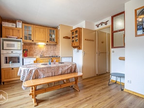 A compact kitchen with wooden cabinets, a dining table with a floral tablecloth, and a bench. - Studio cabin 3 pers South balcony on snow front (Aussois)