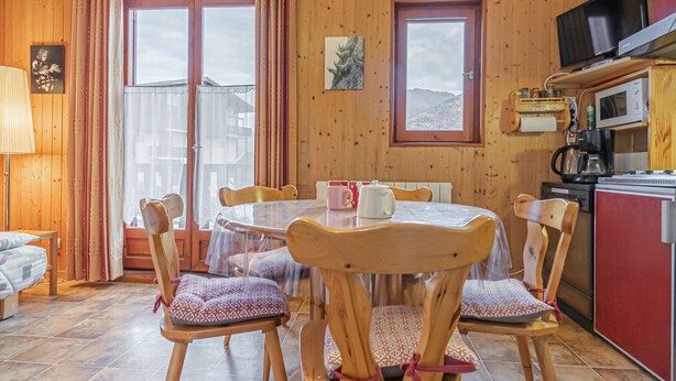 Une pièce chaleureuse aux murs en bois, avec une table à manger ronde, des chaises, un coin cuisine équipé d’un four à micro-ondes et une grande fenêtre donnant sur l’extérieur.