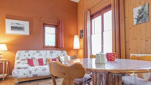 Une pièce chaleureuse avec un mur en bois, un canapé agrémenté de coussins à motifs, une table à manger avec des chaises et une fenêtre avec des rideaux.