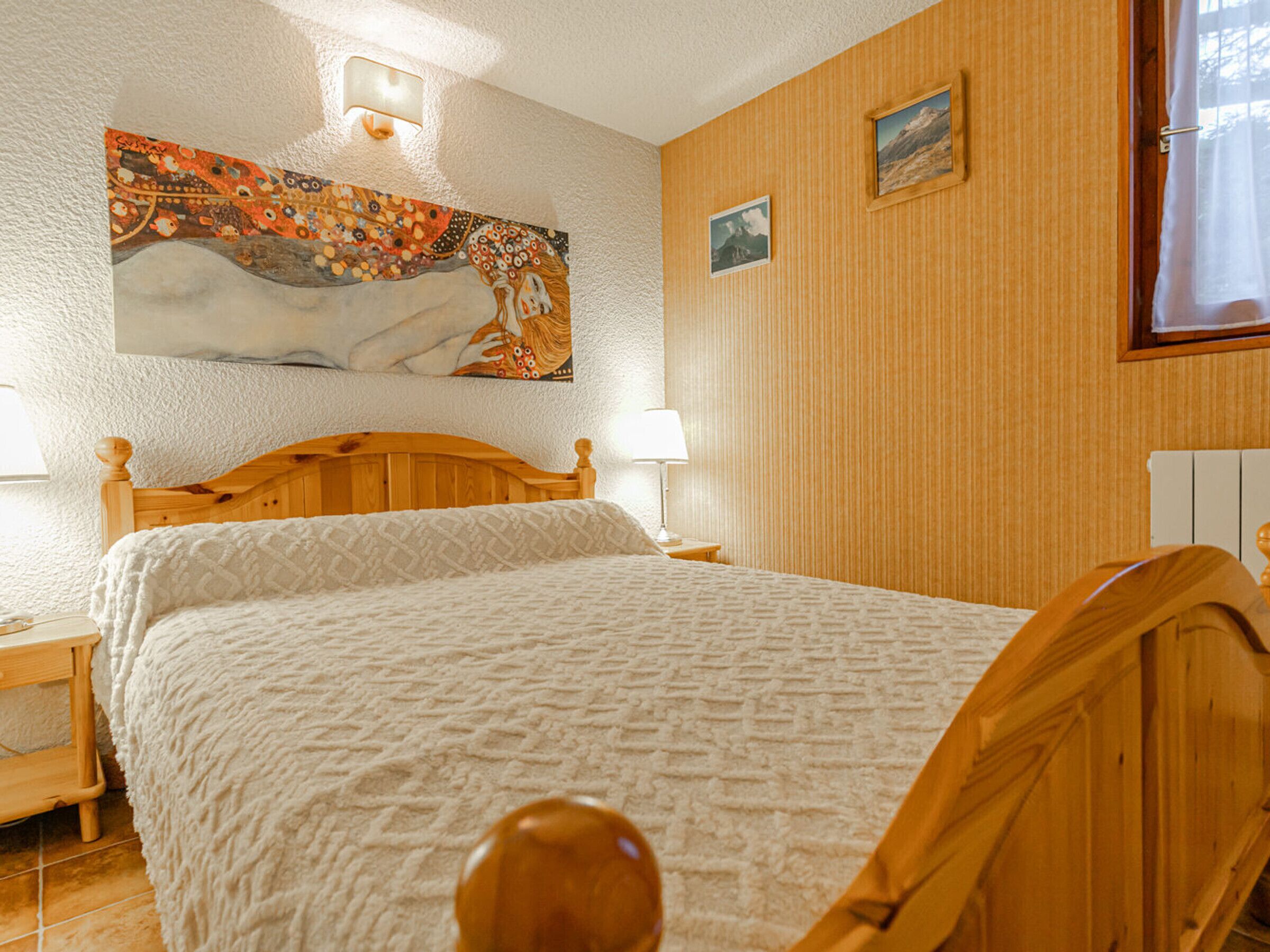 Un dormitorio con una cama de madera, una mesita de noche, una lámpara de pared y un cuadro.