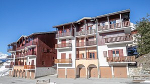 Un hôtel à plusieurs étages doté de balcons, avec une piste de ski en arrière-plan et un ciel dégagé.
