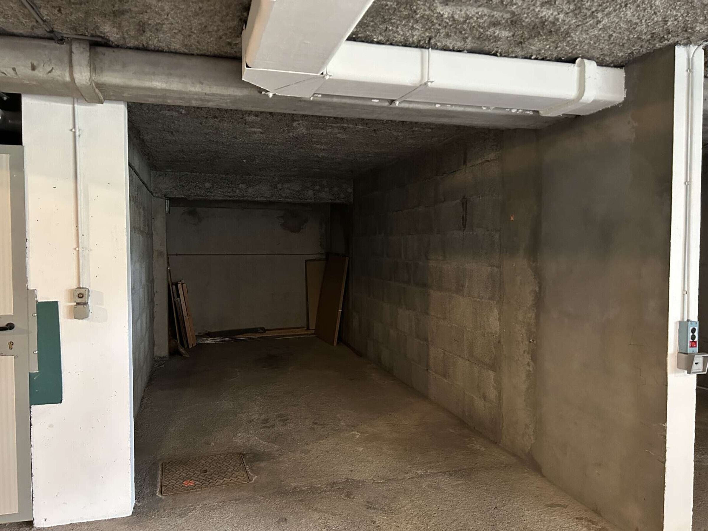 A narrow, unfinished basement with concrete walls and a door leading to a hallway.