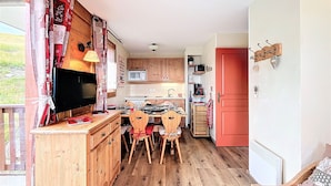 Eine gemütliche Küche mit Holzausbau, einem Esstisch mit Stühlen, einem Fernseher und einer roter Tür.