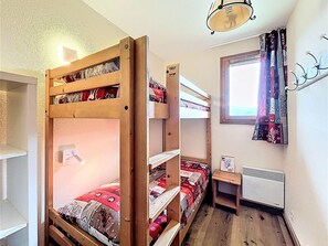 A bunk bed room with a window, a radiator, and a shelf with books.