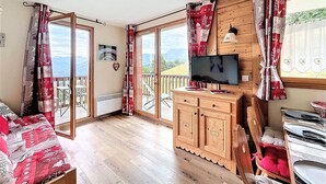 Ein gemütliches Zimmer mit einem Holzbett, einem Fernseher auf einer Holzkommode und einem Balkon mit Bergblick.