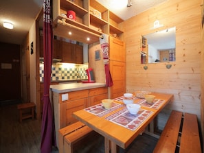 Ein gemütliches Holzhaus mit Küchenbereich, der sich durch eine karierte Spritzschutzwand, einen roten Wasserkocher und einen für das Essen gedeckten Holztisch auszeichnet.