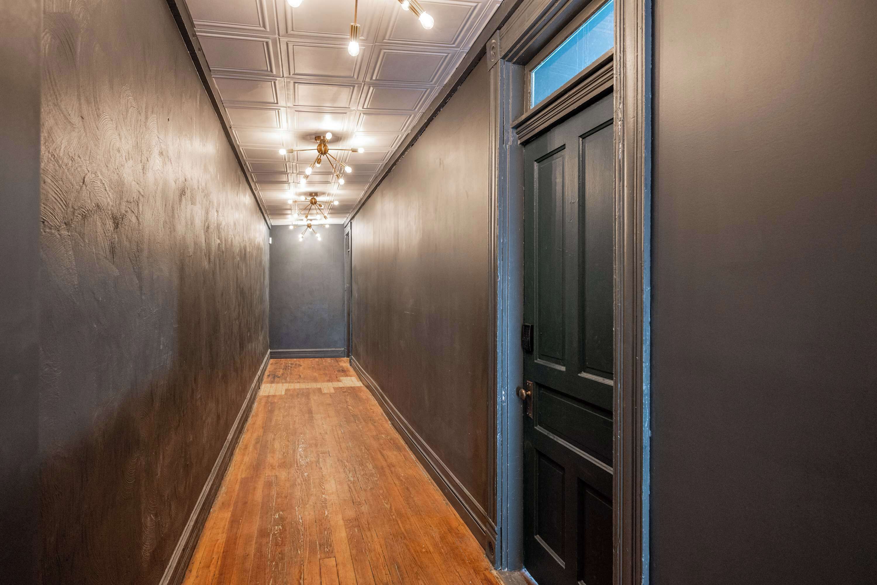 Un pasillo con paredes oscuras, suelo de madera y una puerta con marco azul.
