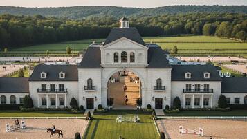 A large equestrian facility with a grand entrance, multiple riding arenas, and a scenic backdrop of hills.