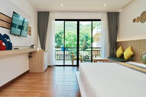 A hotel room with a large bed, a TV mounted on the wall, a balcony with a view of greenery, and a small seating area with a table and chairs. - mar ozo kohtao (Koh Tao)