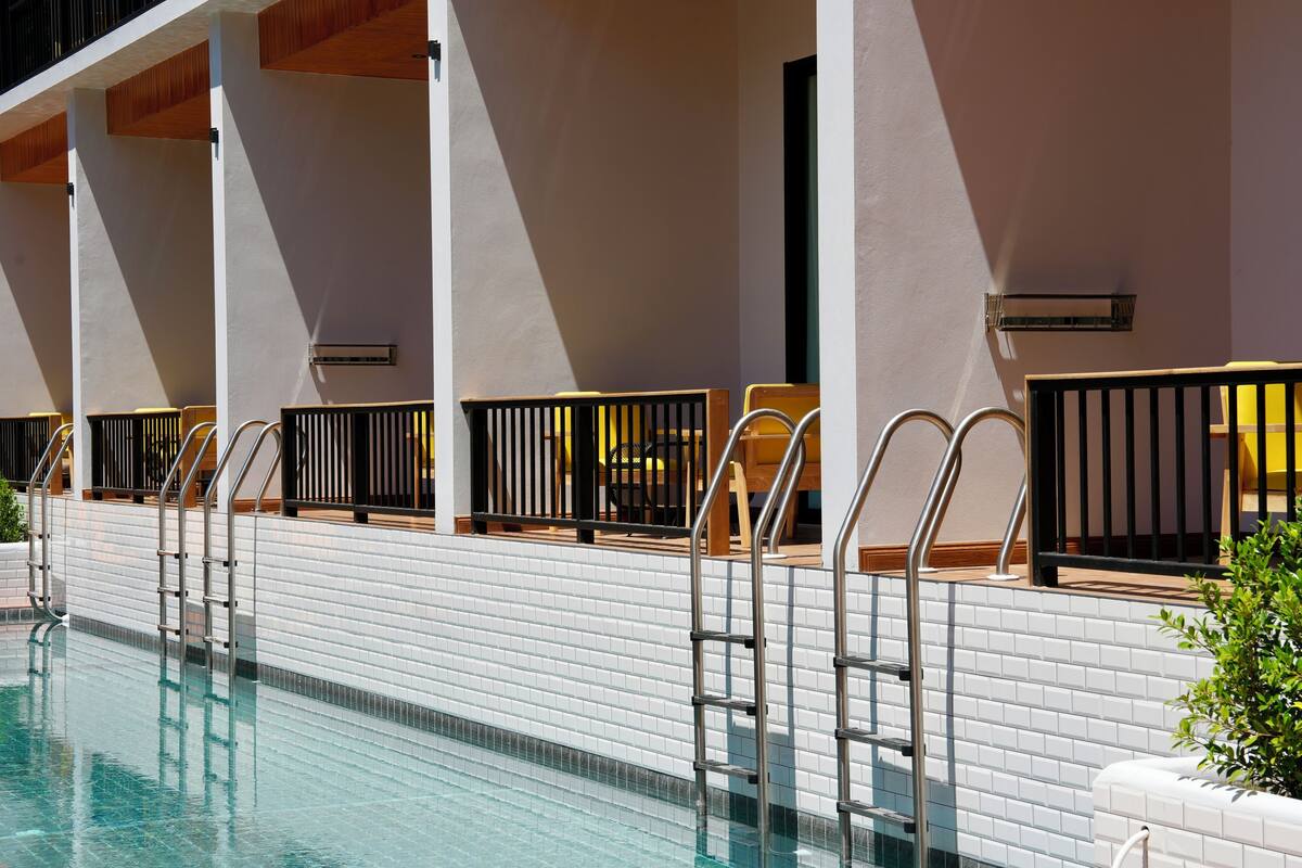 Zona de piscina amb parets de rajola, baranes metàl·liques i cadires de fusta.