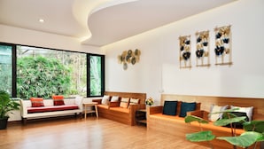 Un salon moderne avec un plancher en bois, deux canapés avec des coussins, une table basse et une grande fenêtre donnant sur un paysage verdoyant.