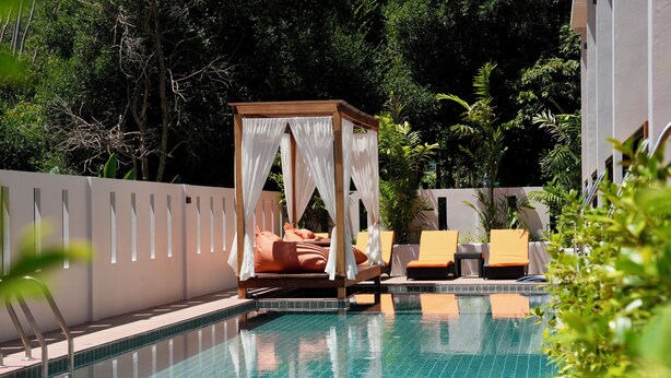 Un espace piscine doté d’un lit à baldaquin, de chaises longues et d’une piscine carrelée.
