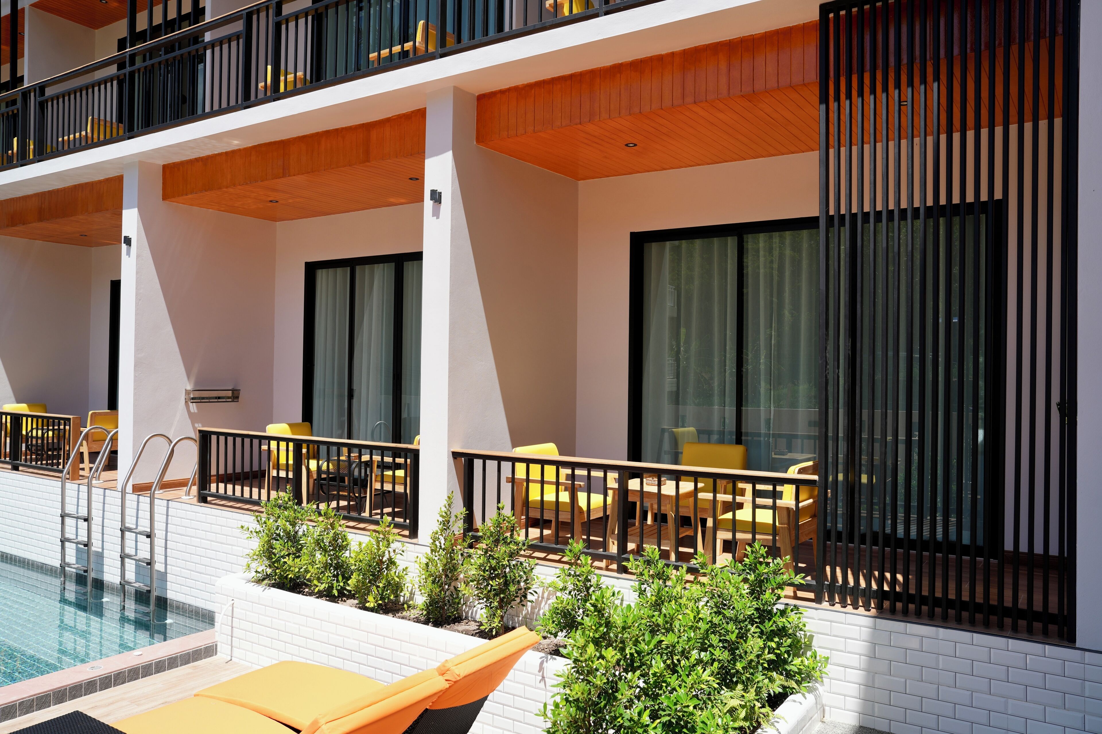 A modern hotel balcony with a pool, outdoor seating, and large windows.