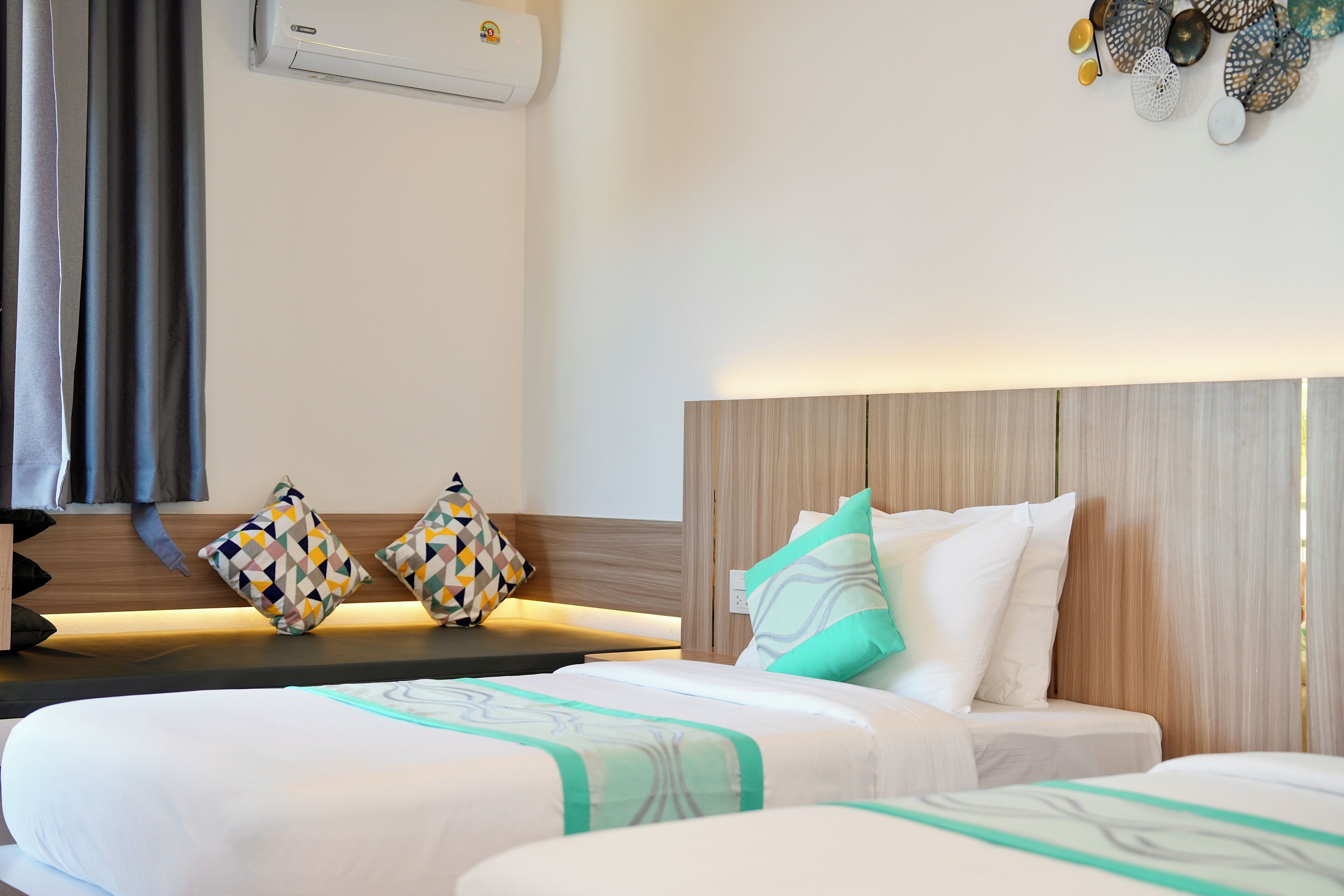 Une chambre d’hôtel avec deux lits, une tête de lit en bois, des coussins décoratifs et un climatiseur fixé au mur.