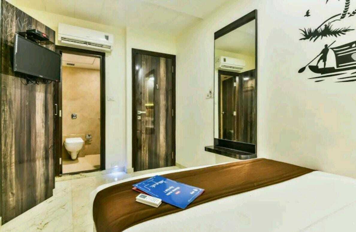 A hotel room with a wooden vanity, a mirror, a bed with a blue book, and a wall decal of a boat.