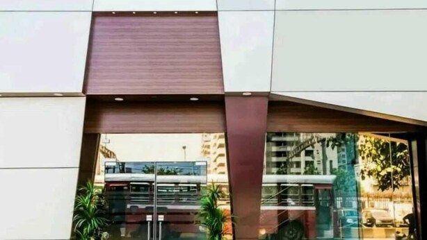 A modern building facade with a geometric design, large windows, and a visible reflection of a bus. - Hotel Palace Residency (Mumbai)