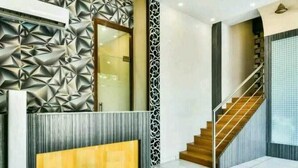 A modern reception area with a geometric wall design, a wooden reception desk, and a staircase leading to another floor. - Hotel Palace Residency (Mumbai)