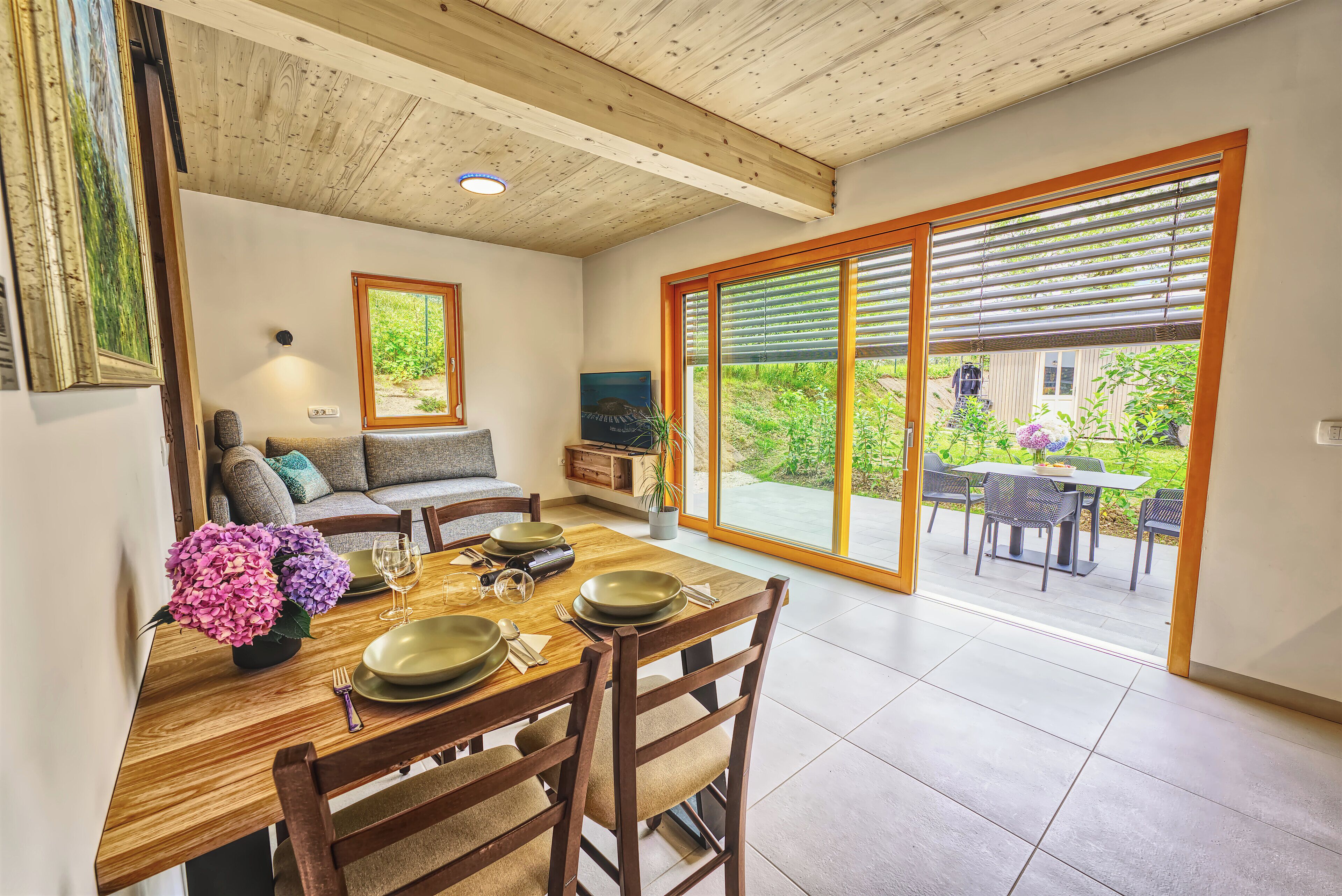 A dining area with a wooden table set for four, a sofa, and a TV in the background.