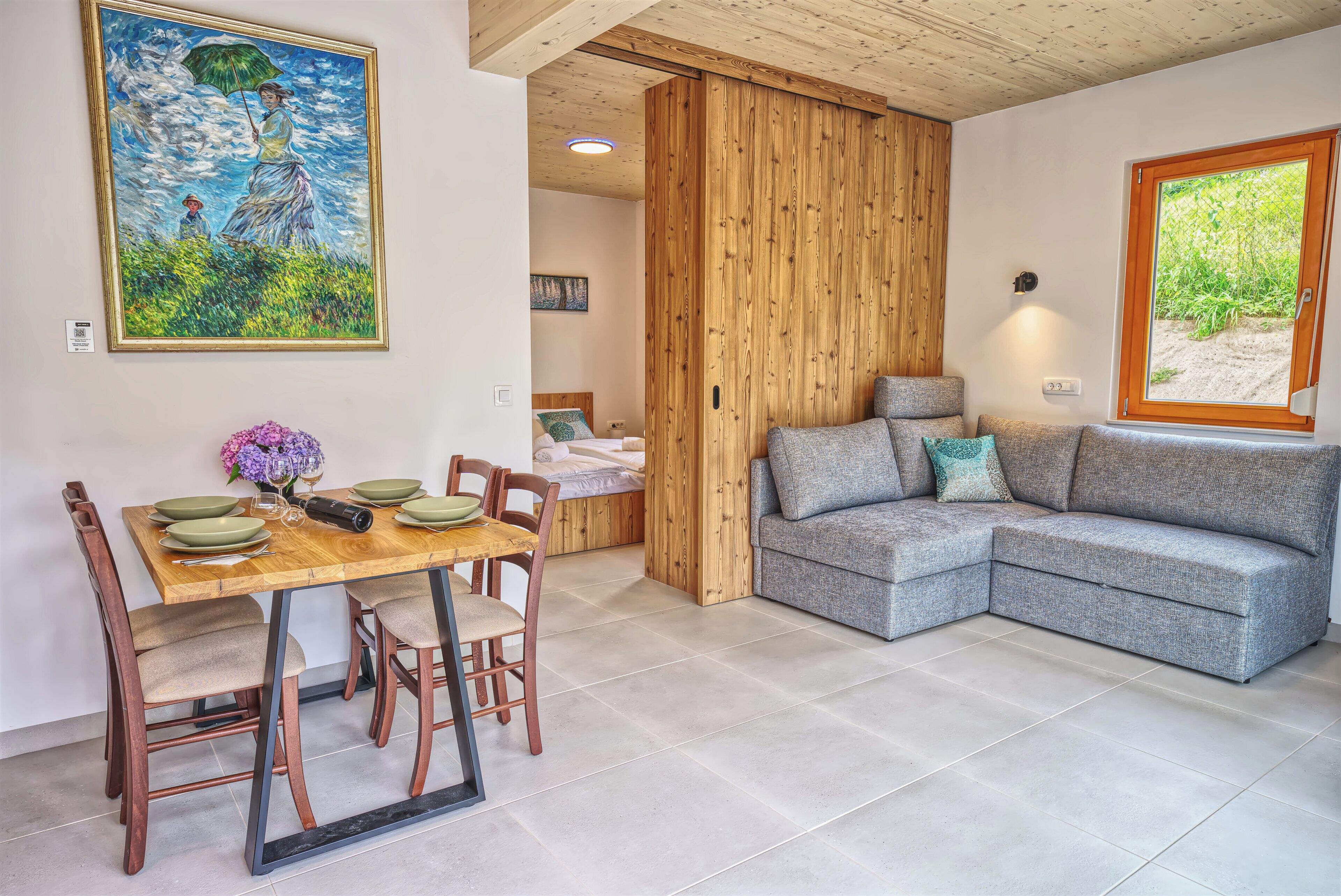 Ein Essbereich mit einem Holztisch, gedeckt für vier Personen, einer grauen Couch und einem großen Gemälde an der Wand.