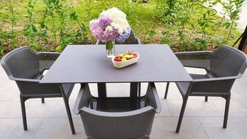 Una mesa con un jarrón de flores y un frutero, rodeada de sillas.