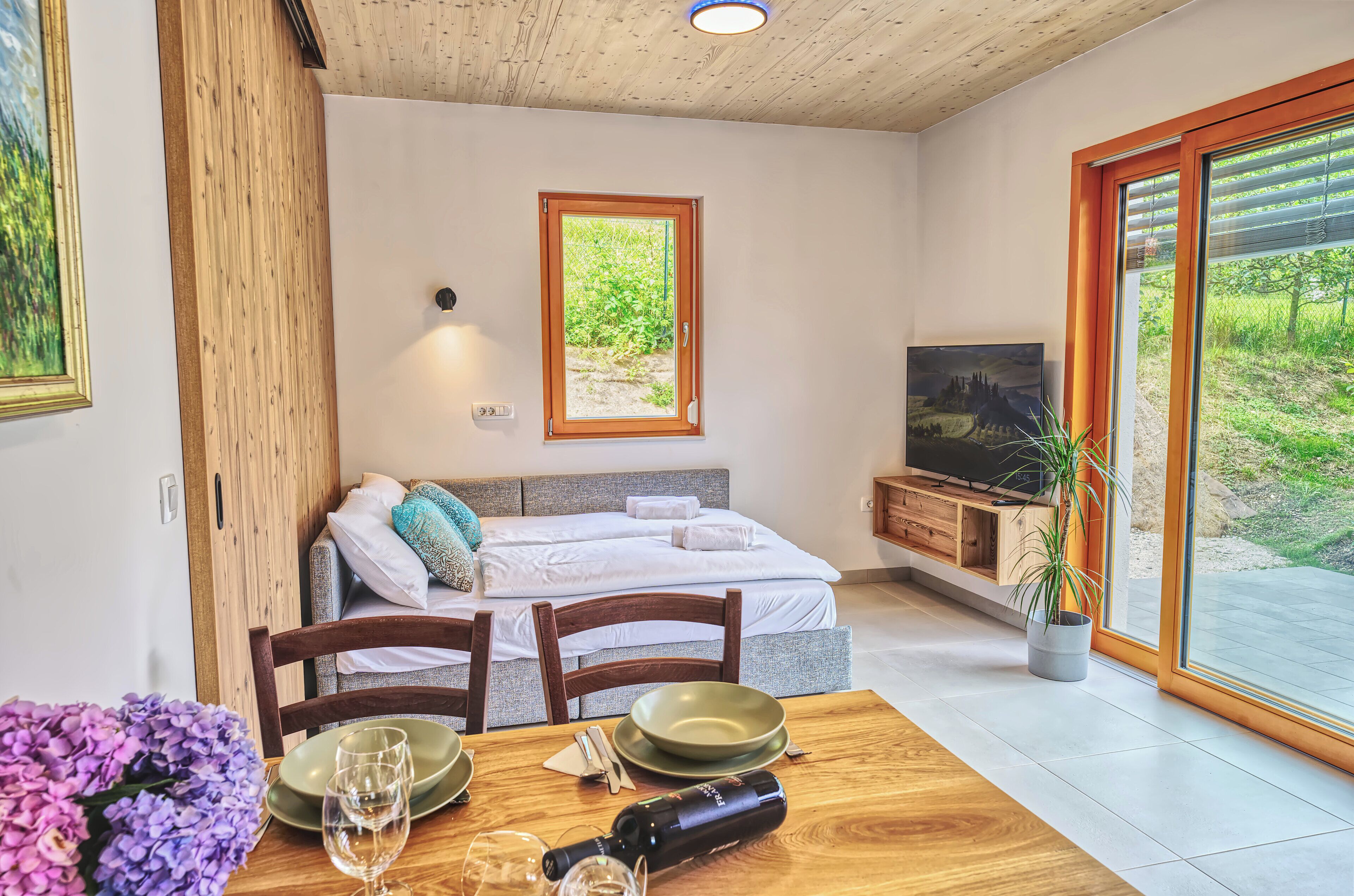 Ein modernes Zimmer mit Bett, Fernseher, Esstisch und großem Fenster.