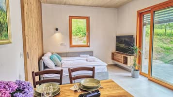 Ein modernes Zimmer mit Bett, Fernseher, Esstisch und großem Fenster.