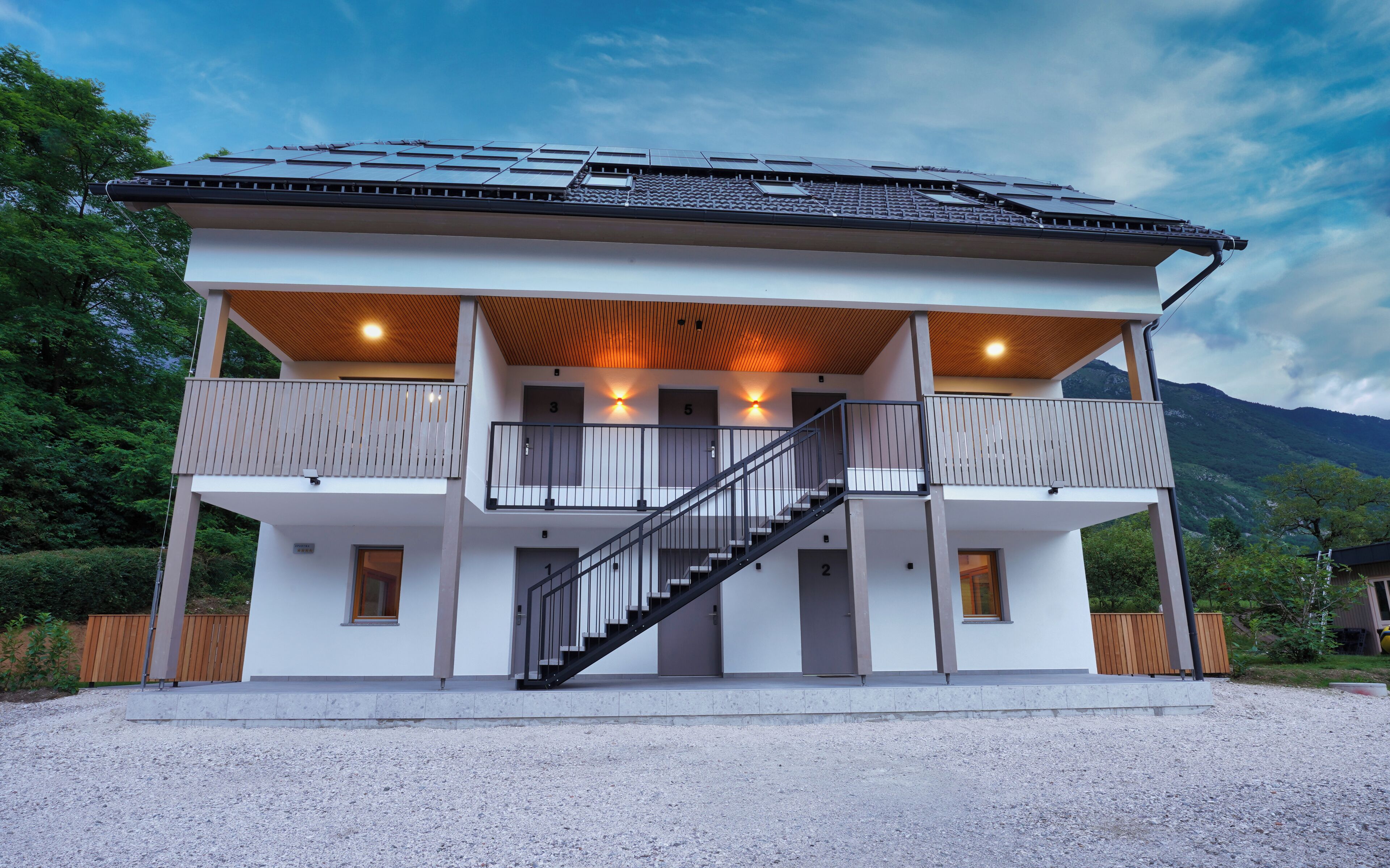 Une maison moderne à deux étages, dotée d’un balcon, d’un escalier et de panneaux solaires sur le toit.