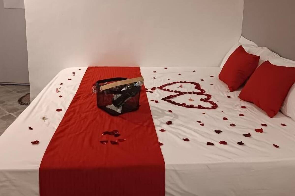 A neatly made bed with a heart-shaped design on the bedspread, red pillows, and a red runner.